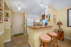 A compact kitchen with a central island, bar stools, and a small dining table.