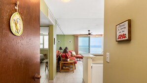 Een kamer met een kitchenette, een eethoek met tafel en stoelen, en uitzicht op zee vanaf een balkon.