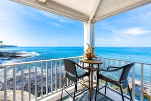 Ein Balkon mit Meerblick, zwei Korbstühle und ein Tisch mit Blumenvase.