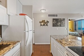 Una cocina con armarios blancos, encimera de granito, refrigerador y estufa. Hay adornos en la pared y una ventana con vistas.