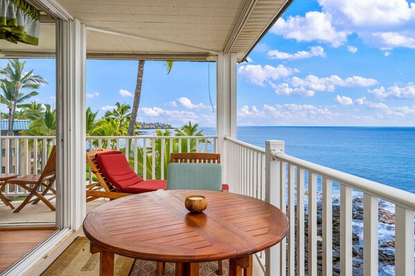 Une terrasse en bois avec une table et des chaises, donnant sur une plage bordée de palmiers et sur l’océan.