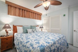 Ein Schlafzimmer mit einem Bett, zwei Nachttischlampen, einem Deckenventilator, einem Fenster mit Jalousien und einer Tür.