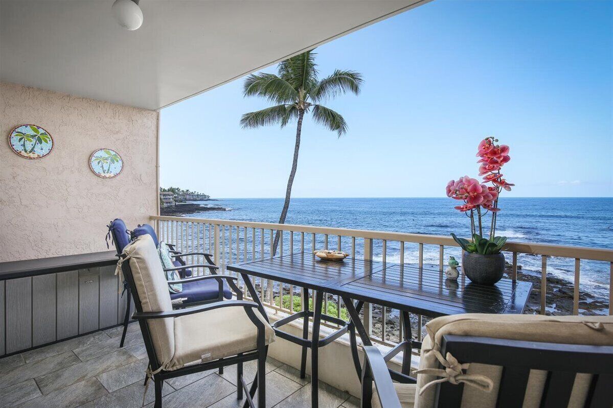 A balcony with a view of the ocean, featuring a table, chairs, and a potted plant.