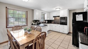 A kitchen with white cabinets, a black refrigerator, and a wooden dining table with chairs. - Shadow Lane Tailgate House - Newly Remodeled (Green Bay)