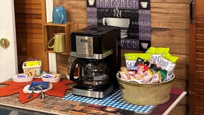Preparación para el desayuno con una cafetera, un cartel que dice "FRESHLY" y un cuenco de aperitivos.