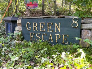 A sign for 'GREEN ESCAPE' with a rustic stone wall and greenery around it.