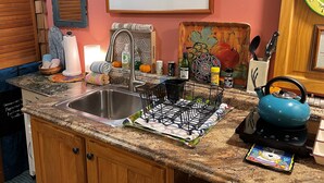 Una cocina con encimera de granito, pileta de acero inoxidable y una tetera azul.
