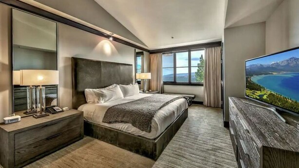 Habitación de hotel moderna con una cama grande, televisión y vistas a un lago.