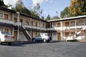 Un motel de varios pisos con una escalera central, espacios de estacionamiento y cielo despejado.
