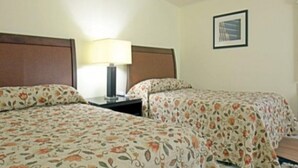 Une chambre d’hôtel avec deux lits, une table de chevet, une lampe et un tableau encadré au mur.