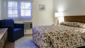 Une chambre à coucher avec un lit, une chaise, un bureau et une fenêtre avec des stores.