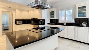 Una cocina moderna con armarios blancos, encimera negra y campana extractora de acero inoxidable.