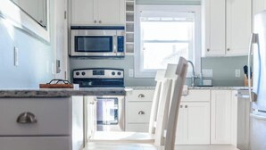 A modern kitchen with white cabinets, a stainless steel refrigerator, a double oven, and a dining area with a white table and chairs. - Newport's favorite Neighborhood 3bed (Newport)