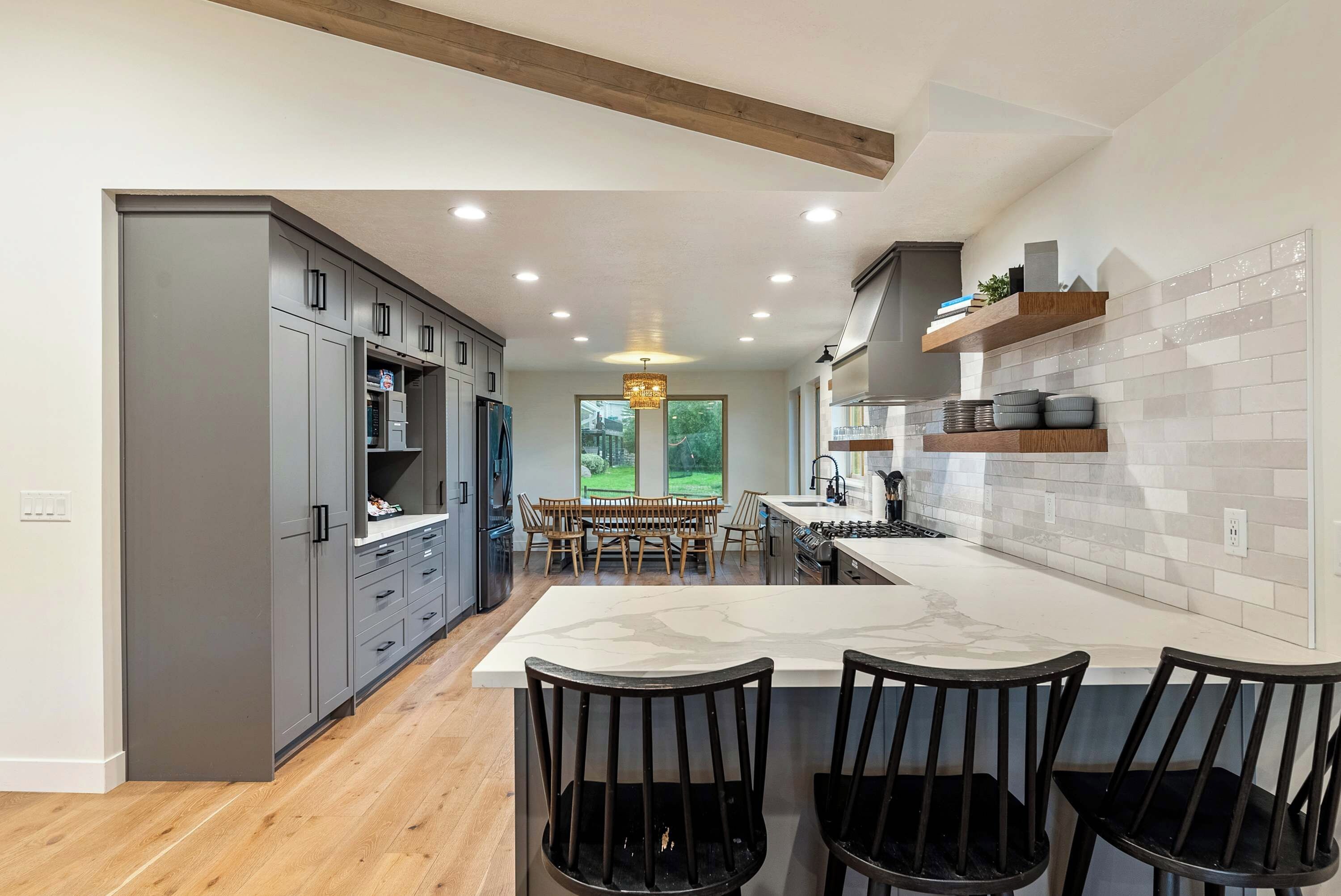Una cocina moderna con armarios grises, encimera de mármol y comedor con sillas de madera.