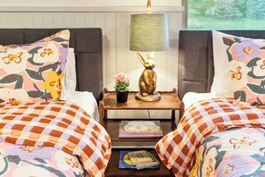 Habitación de hotel con dos camas, una mesita de noche con una lámpara y una figurita de conejo, y una ventana con vistas a árboles.