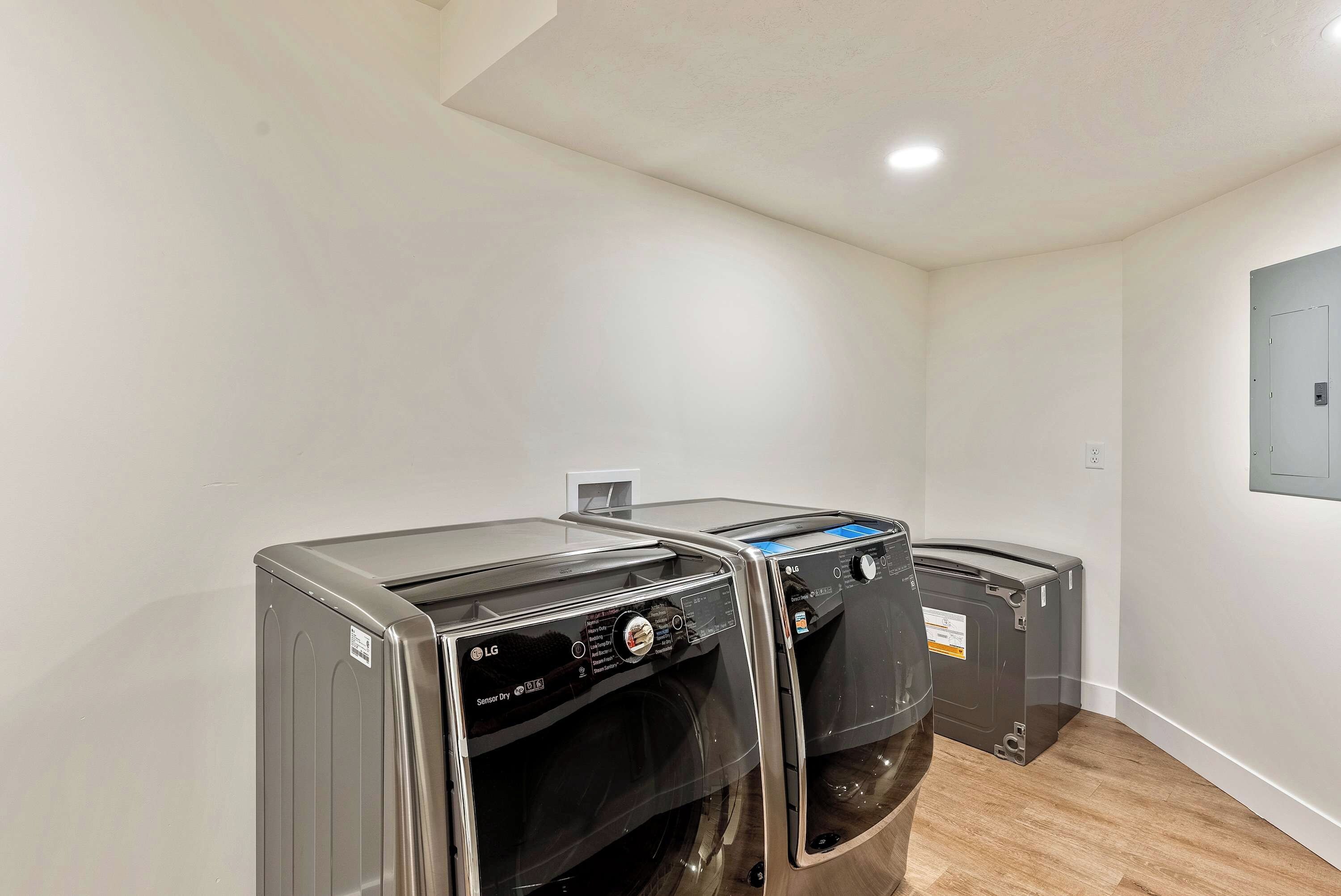 A laundry room with two LG washing machines, a white wall, and a wooden floor.