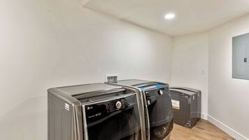 A laundry room with two LG washing machines, a white wall, and a wooden floor.