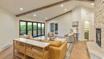 A spacious living room with a large window, a fireplace, and a kitchen area.