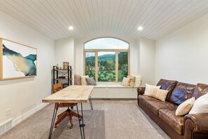 Una habitación con un ventanal grande, una mesa de madera, un sofá de cuero y una estantería.