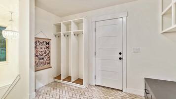 A hallway with a white door, a coat rack with hangers, and a patterned wall hanging.