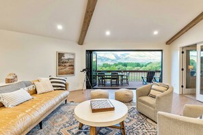 Una sala de estar con un sofá de cuero, una mesa redonda de centro y vista a una terraza con mobiliario exterior.