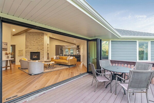 Una sala de estar moderna con chimenea, un comedor con mobiliario de exterior y vistas al paisaje.