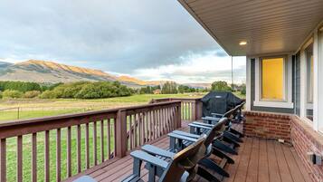 A covered outdoor deck with a barbecue grill, wooden chairs, and a view of a mountainous landscape.