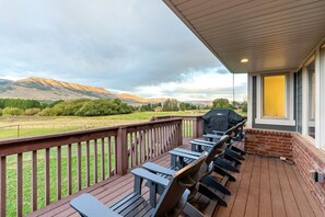 A covered outdoor deck with a barbecue grill, wooden chairs, and a view of a mountainous landscape. - Horseshoe Haven (Eden)