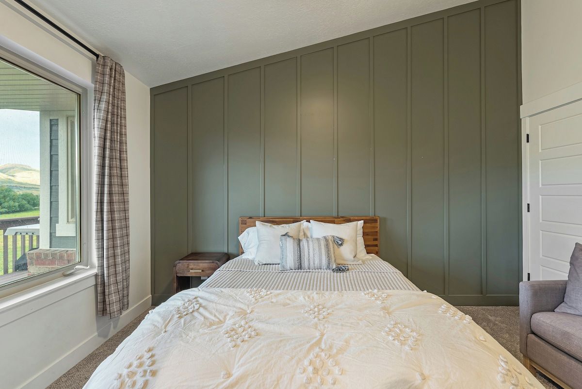 Un dormitorio con una cama grande, cabecera de madera, mesita de noche, ventana con cortinas y vistas al exterior.