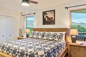 A bedroom with a large bed, a painting of a horse, and a view of mountains through the window.