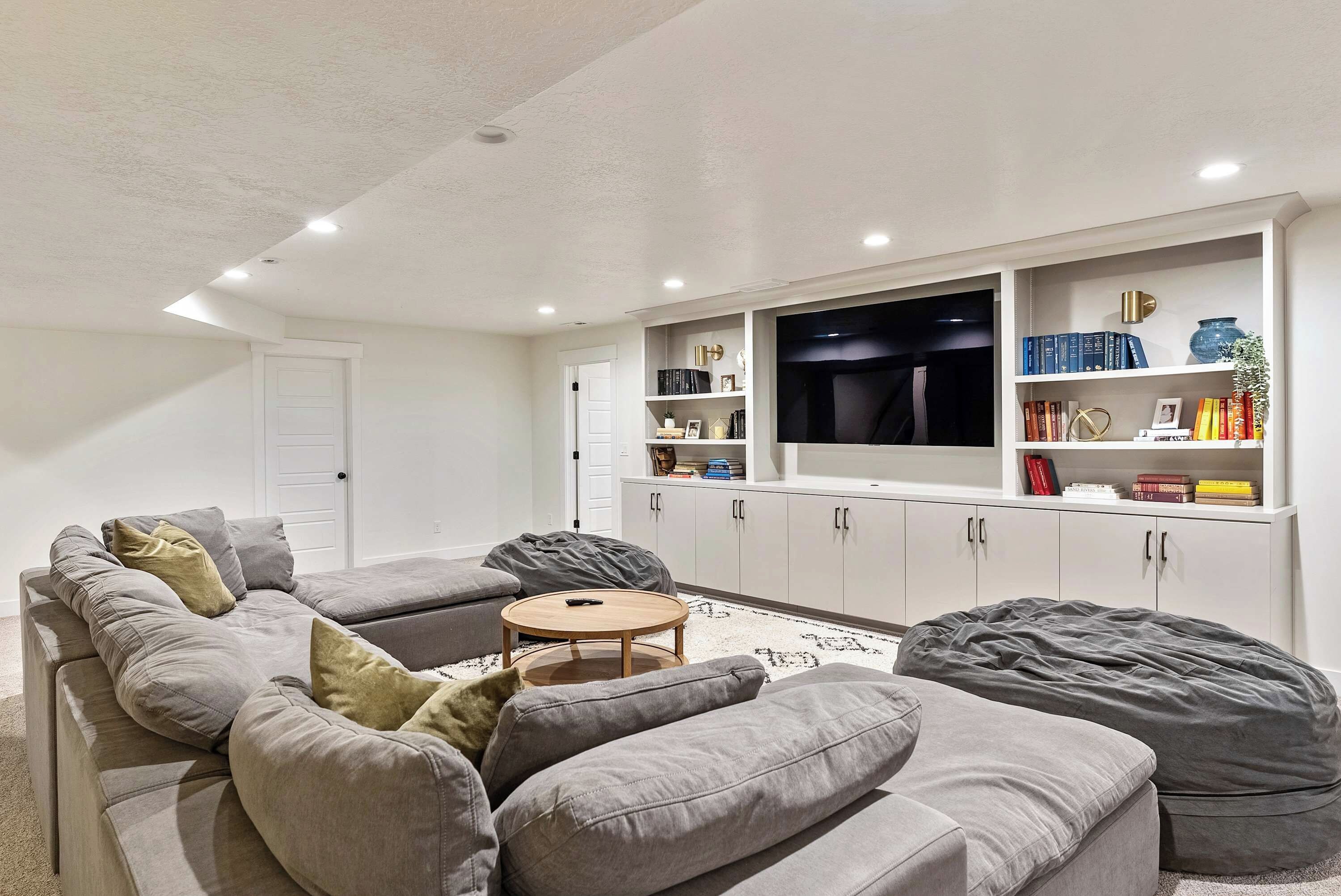 A modern living room with a grey sectional sofa, a round coffee table, and a flat-screen TV mounted on a white wall.