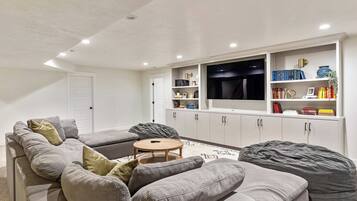 A modern living room with a grey sectional sofa, a round coffee table, and a flat-screen TV mounted on a white wall.