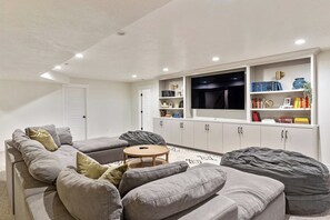 A modern living room with a grey sectional sofa, a round coffee table, and a flat-screen TV mounted on a white wall.