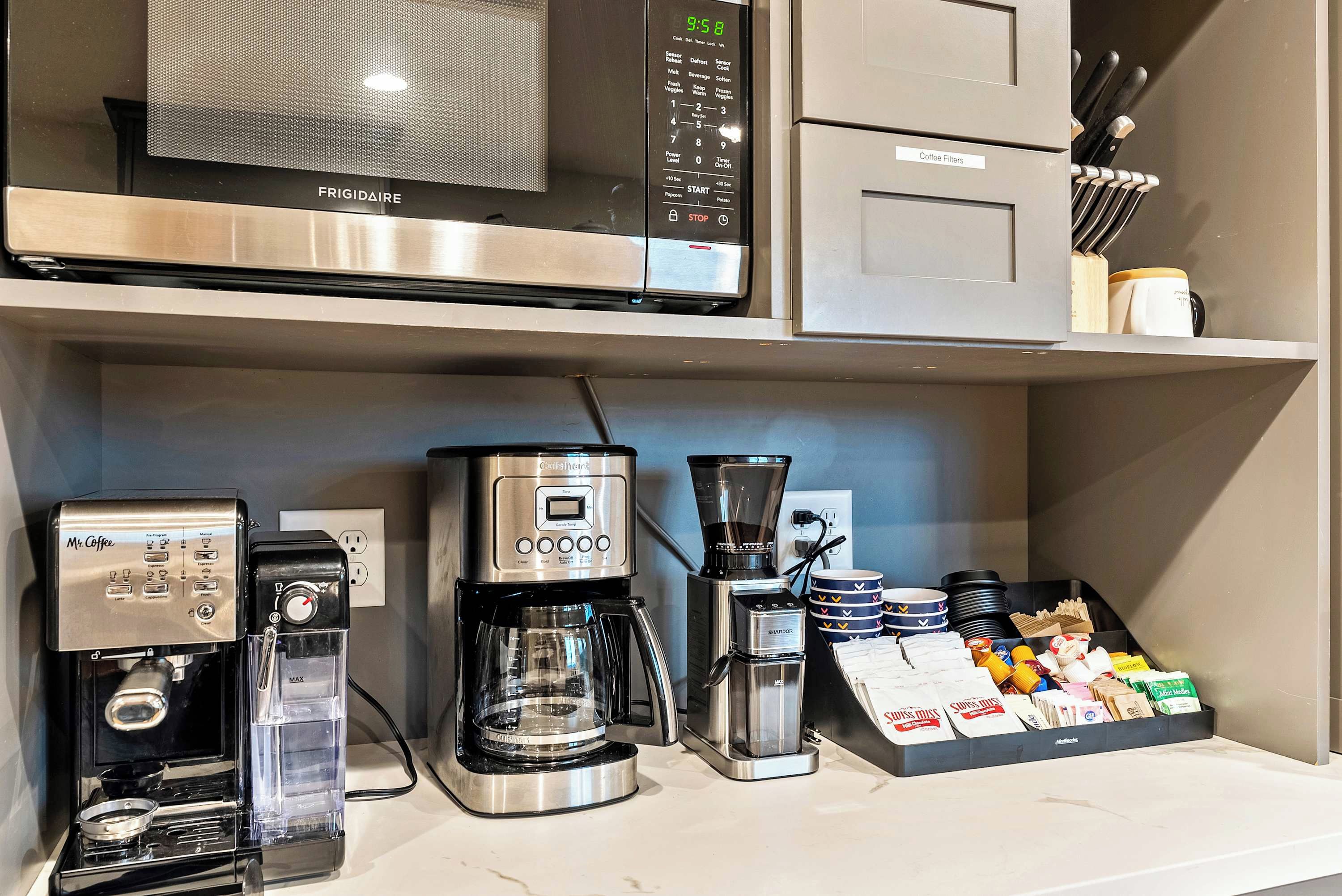 Eine Küchenzeile mit einer Frigidaire-Mikrowelle, einer Kaffeemaschine und einem Kaffeemühle.