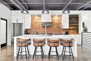 Une cuisine moderne dotée d’un îlot central, de tabourets de bar, d’un mur d’accent en briques et d’appareils électroménagers en acier inoxydable.