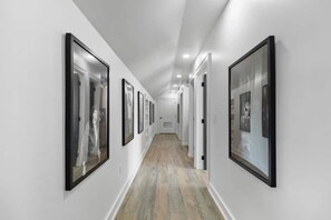 A hallway with framed pictures on the walls, a wooden floor, and white walls.