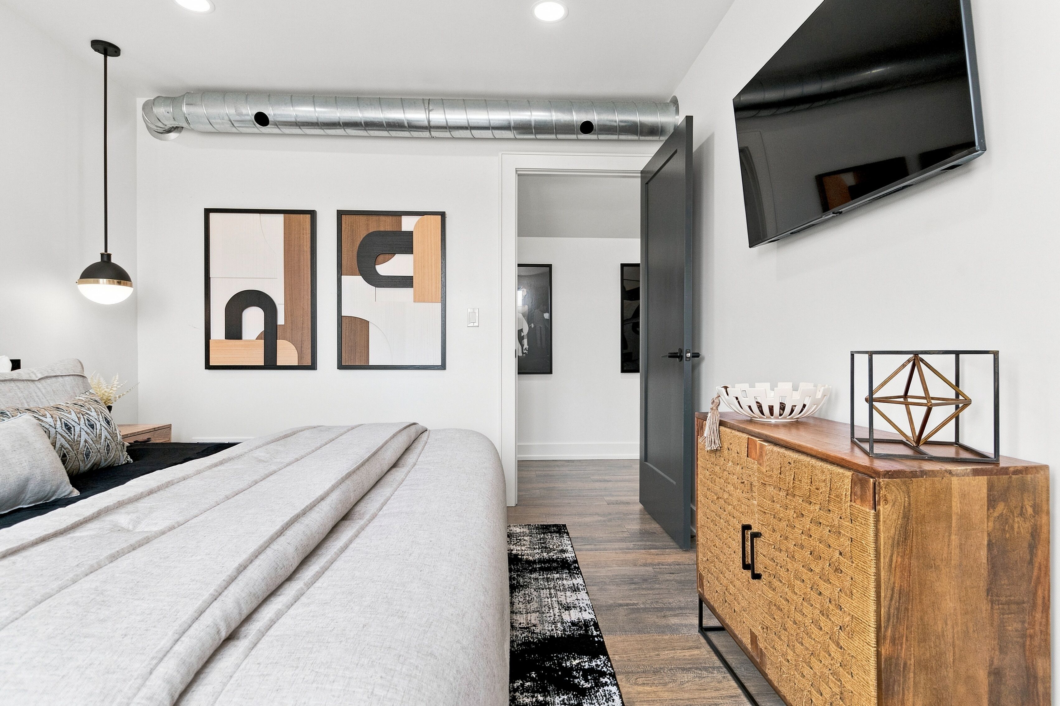 A modern bedroom with a bed, a dresser, a TV mounted on the wall, and artwork.