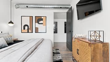 A modern bedroom with a bed, a dresser, a TV mounted on the wall, and artwork.