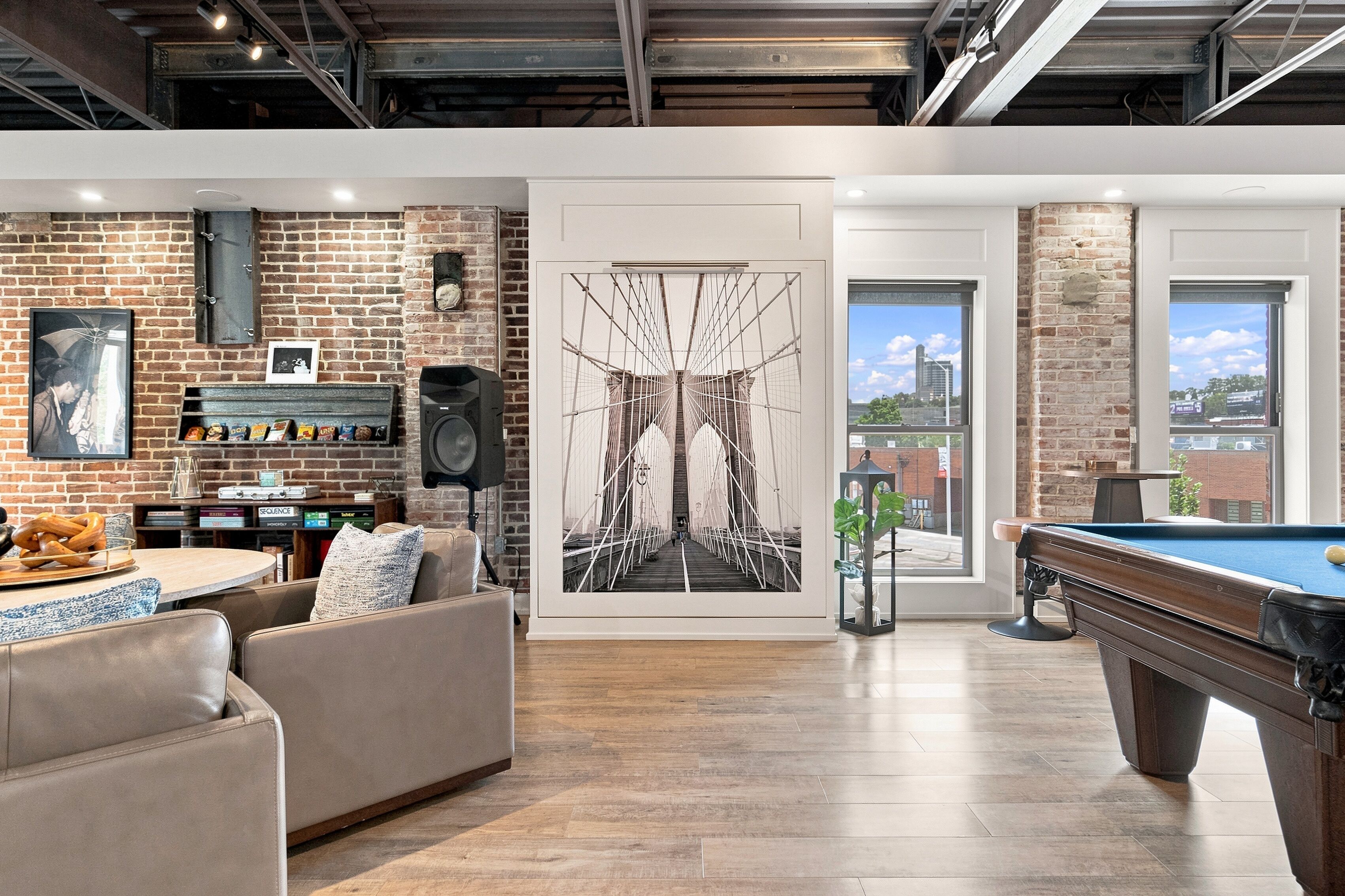 A modern living room with a pool table, a brick wall with a framed picture, and a large window.