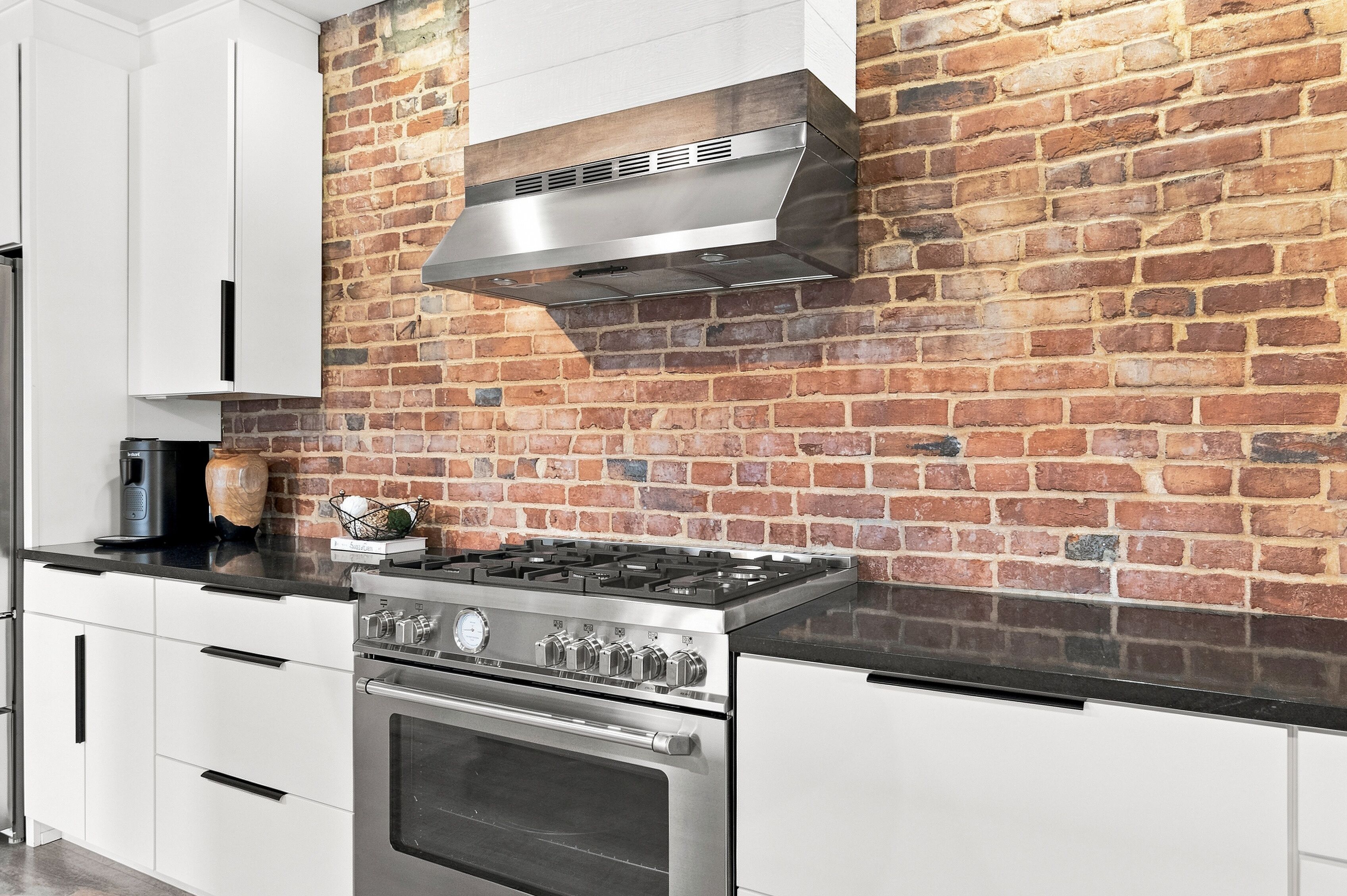Een keuken met een bakstenen muur, roestvrijstalen apparatuur en witte kasten.