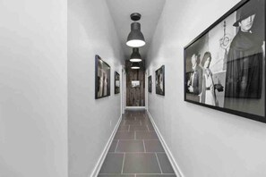A hallway with framed pictures on the walls, a tiled floor, and a hanging light fixture.