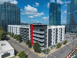 A multi-story building with balconies, a red accent wall, and a parking lot in front.