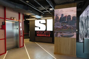 Un vestíbulo de hotel con un ascensor, un gran letrero iluminado que dice 'RESORTS NASHVILLE' y una vista de la ciudad en la pared.