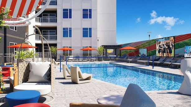 A swimming pool with lounge chairs and umbrellas, a modern building with large windows, and a mural on the side.