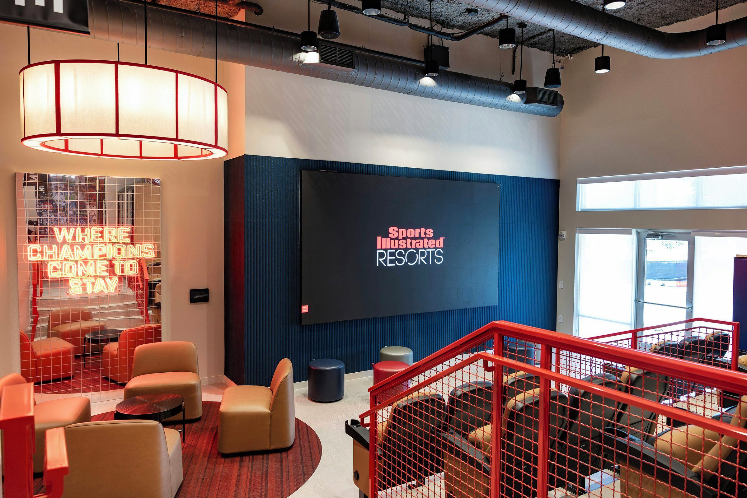 A modern hotel lobby with a large screen displaying 'Sports Illustrated Resorts' and a neon sign reading 'Where Champions Come To Stay.'