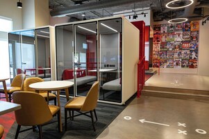 Un espacio de oficina moderno con divisiones de vidrio, asientos cómodos y una pared decorada con revistas deportivas.