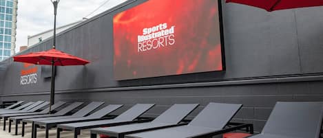Una fila de tumbonas con una pantalla grande mostrando 'Sports Illustrated Resorts' en una pared de edificio.