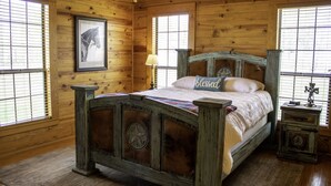 A wooden cabin bedroom with a four-poster bed, a framed horse picture, and a bedside table with a clock. - Charming Country Cabin in Quaint Texas Town (Fayetteville)