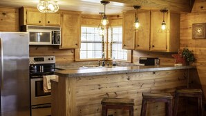 A kitchen with wooden cabinets, stainless steel appliances, a central island with stools, and pendant lighting. - Charming Country Cabin in Quaint Texas Town (Fayetteville)