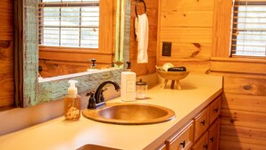 A wooden cabin bathroom with a round sink, a mirror, and wooden cabinets. - Charming Country Cabin in Quaint Texas Town (Fayetteville)